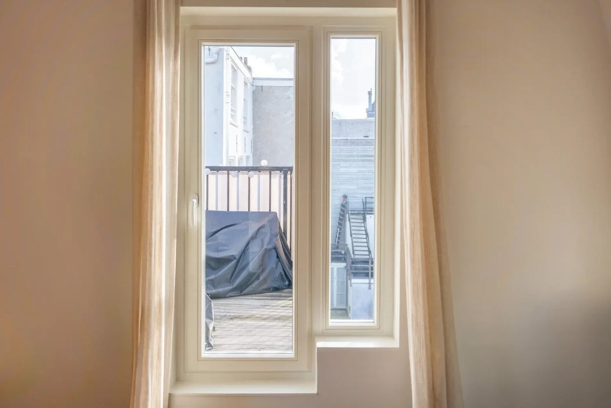 White casement window with a fixed side light, framed by linen curtains